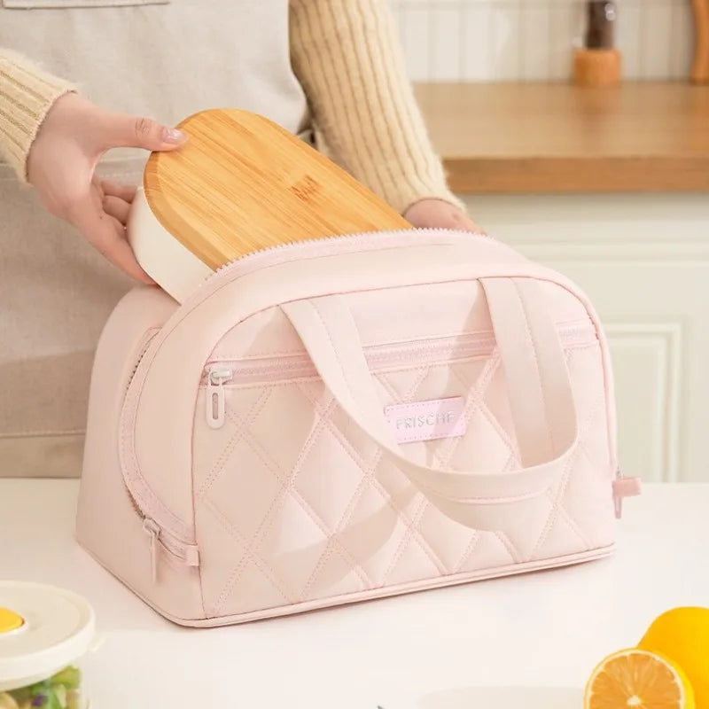 A pink quilted insulated lunch tote is shown next to a wooden lid, with a person's hand holding the item.