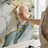 A hand wipes a gold leaf marble wall sticker design featuring gray and white marbled patterns on a vertical surface.
