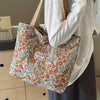 A person holds a beige corduroy tote bag with floral accents in a light gray sweater.
