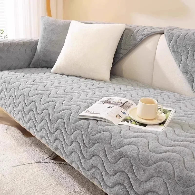 A gray plush anti-slip sofa cushion mat with white pillows and a cup of tea on a light-colored sofa.