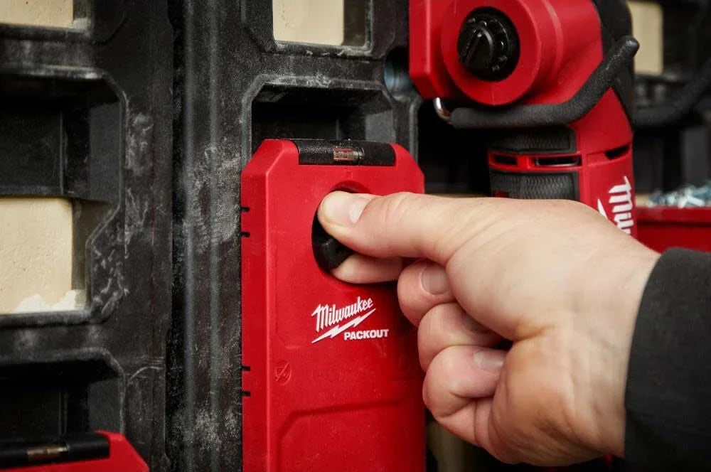 A hand is using a red Milwaukee PACKOUT magnetic bin for tool storage.