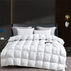 A white quilted comforter with white pillows is displayed on a dark bed against a gray wall.
