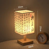 A square Chinese style table lamp with a woven linen shade sits on a wooden base, illuminated by warm light.