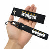 Black nylon keychain with embroidered wanted text and gold stars, held in a hand.