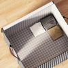 A foldable quilt storage bag with handles shown open on a wooden floor, featuring gray and black patterned fabric.