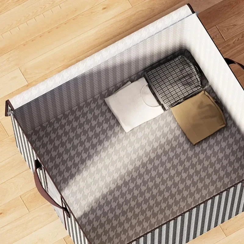 A foldable quilt storage bag with handles shown open on a wooden floor, featuring gray and black patterned fabric.