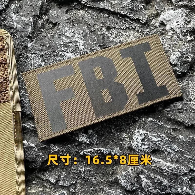 A dark olive tactical morale patch featuring the embroidered letters FBI on a rough stone background.