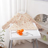 A light floral patterned long-sleeve baby bib is displayed on a white table against a white background.