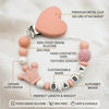 A pink silicone baby pacifier clip featuring a heart shape and alphabet beads for a custom name