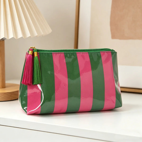 Sac de maquillage rayé vert et rose avec franges dorées et fermeture éclair sur une surface blanche.