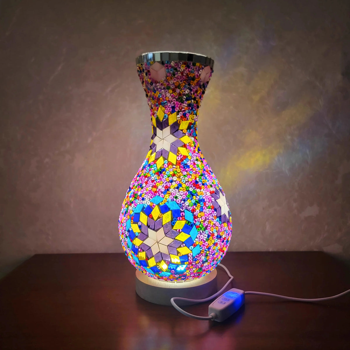 A handcrafted Turkish mosaic table lamp with a vibrant, colorful glass base and a metallic top, illuminated by a warm LED glo