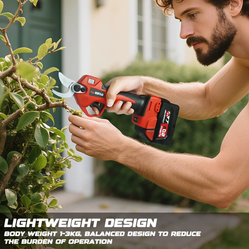 A man uses a red cordless electric pruning shear tool on a green shrub.