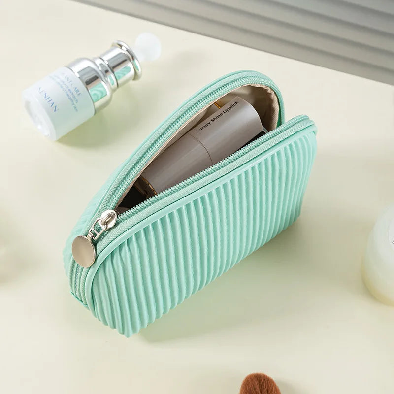 A light mint green zippered makeup bag set with a cylindrical product tube and a brush visible on a pale surface.