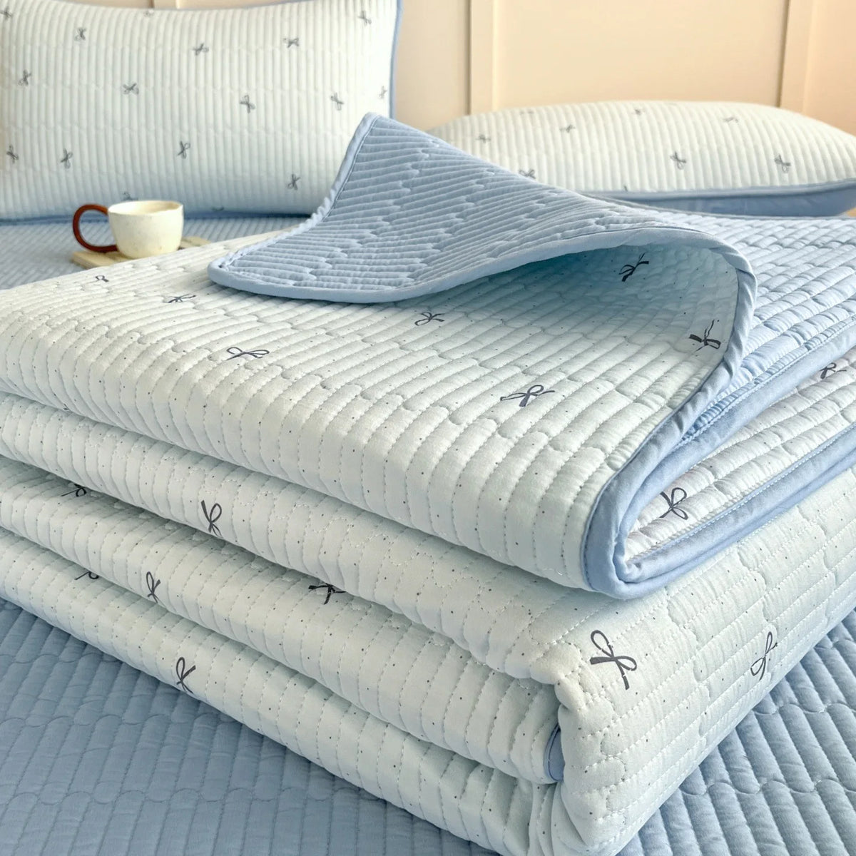 Light blue quilted bedspread and pillows with a subtle floral pattern on a bed.