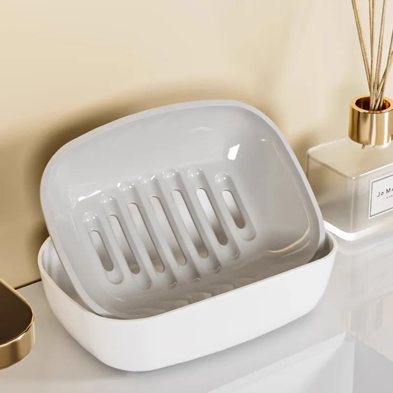A white double-layer draining soap dish with a non-slip base is shown on a light surface.