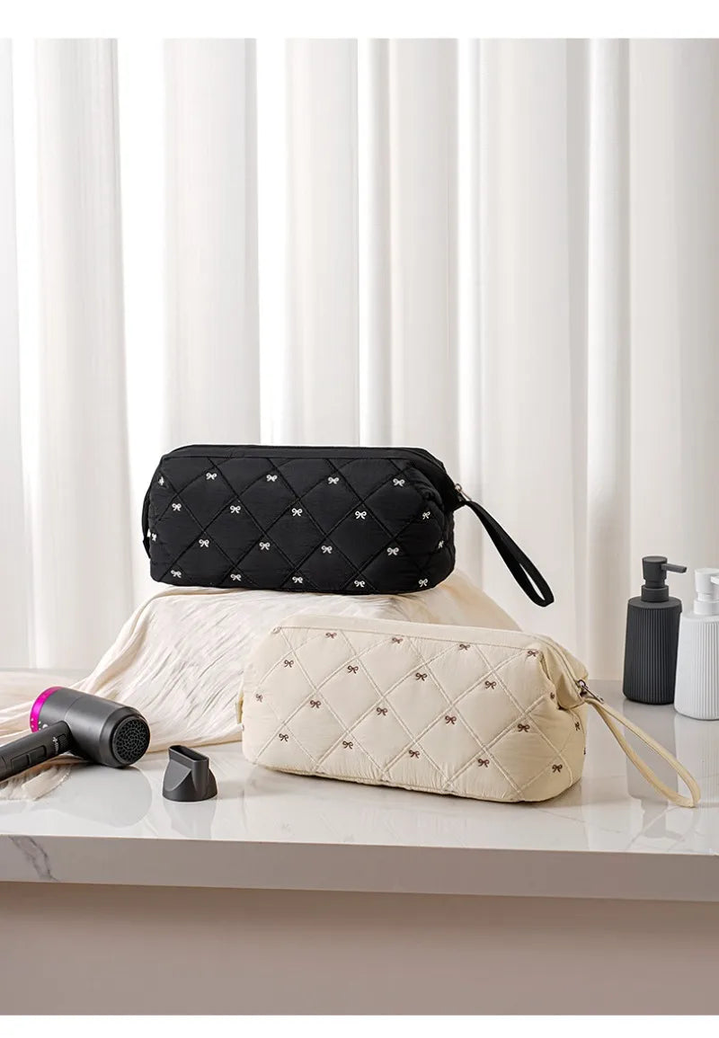 Two fabric storage bags, one black and one beige, are displayed on a white surface next to a hair dryer.