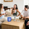 Three adults laughing while playing a drinking game with cards on a table