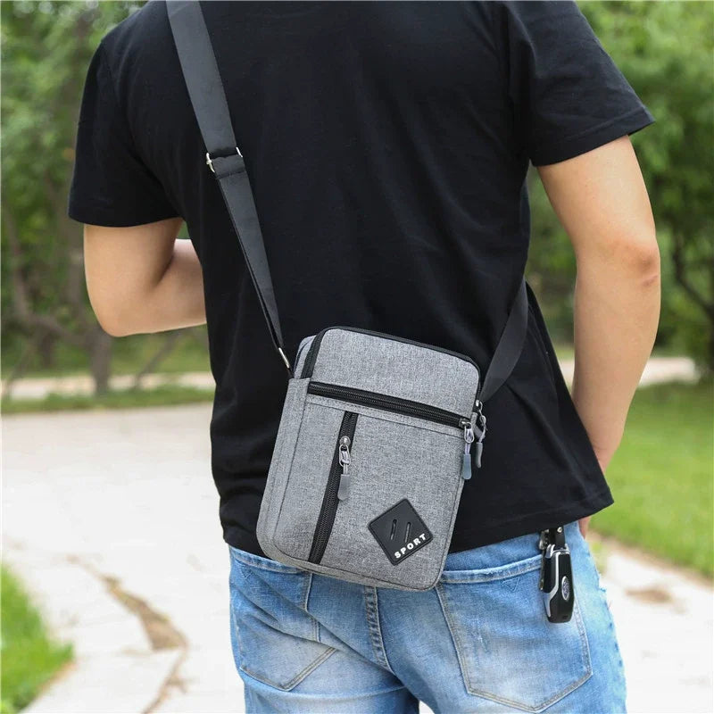 A man wearing a black t-shirt is holding a gray lightweight crossbody sling bag with multiple zip pockets.