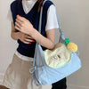 A person wearing a white shirt and navy vest holds a light blue nylon messenger bag with a yellow charm.