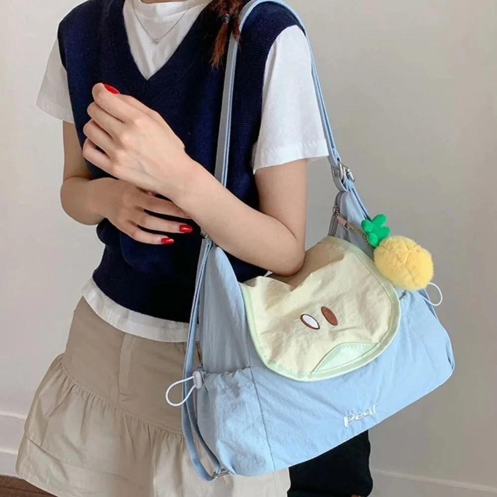 A person wearing a white shirt and navy vest holds a light blue nylon messenger bag with a yellow charm.