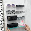 A hand displays a clear acrylic wall-mounted display shelf holding various pairs of eyeglasses and sunglasses.