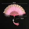 Pink folding fan with lace trim and golden edge, shown against a black background.