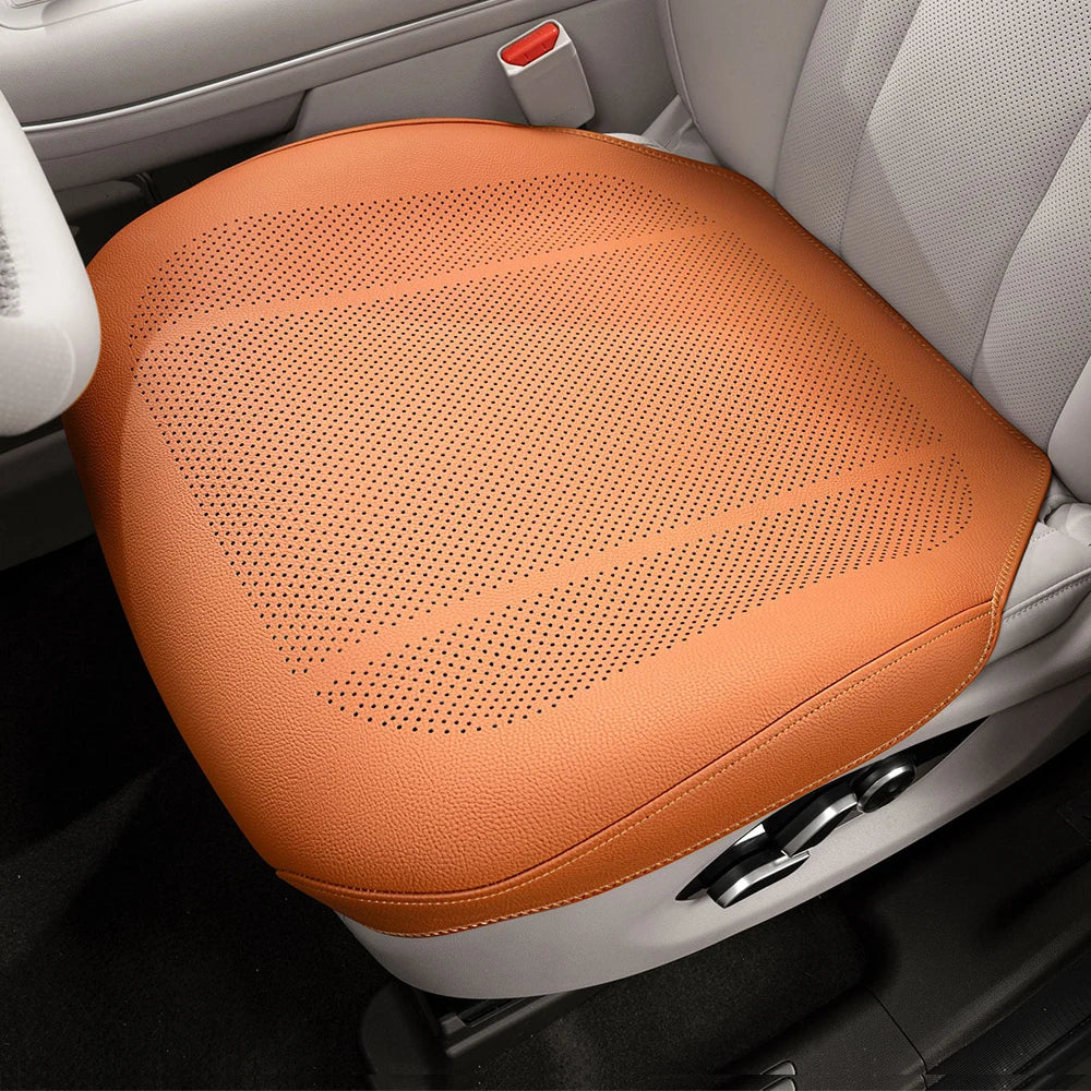 An orange breathable leather car seat cushion is shown placed in the interior of a vehicle.