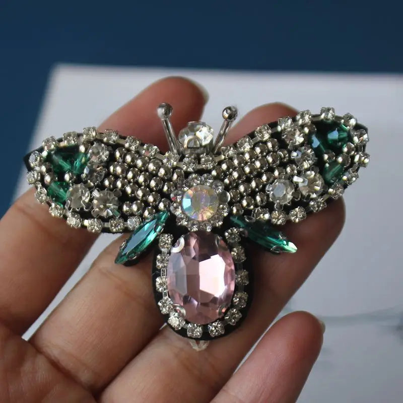 A handcrafted rhinestone bee sew-on patch featuring green and pink stones on a silver backing.