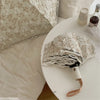 A white lace double-layer folding umbrella is shown resting on a white table next to pillows.