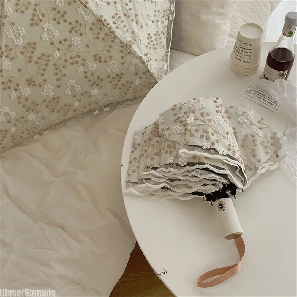 A white lace double-layer folding umbrella is shown resting on a white table next to pillows.
