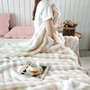 A person is wrapped in a fluffy cream colored gradient bubble fleece throw blanket indoors.