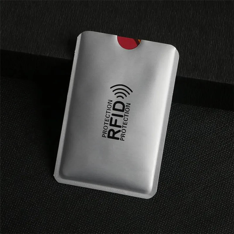 A silver aluminum card holder with an RFID protection symbol on a dark surface.
