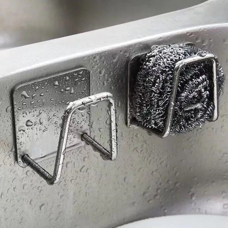 Stainless steel sponge holder with a mesh scrubber attached, mounted on a sink surface.