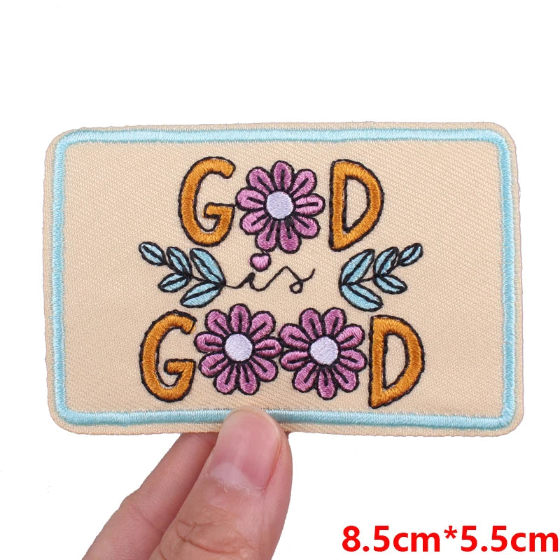 A beige embroidered patch featuring the letters G O D surrounded by pink and blue floral designs.