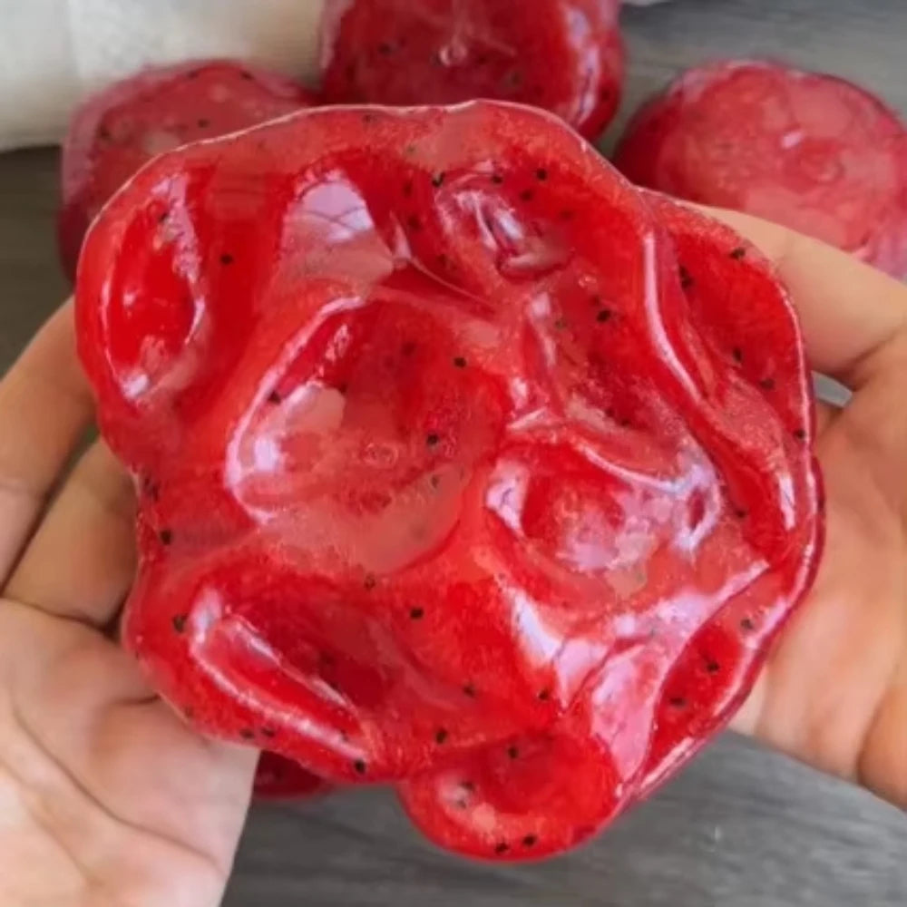 Une main tient un jouet anti-stress en forme de pastèque rouge vif et moelleux.