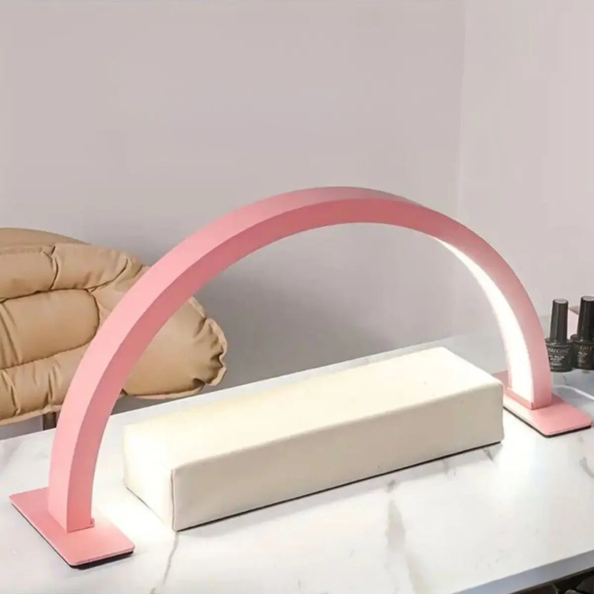 A pink half-moon LED arc desk lamp illuminates a white rectangular surface for nail art or lash extensions.