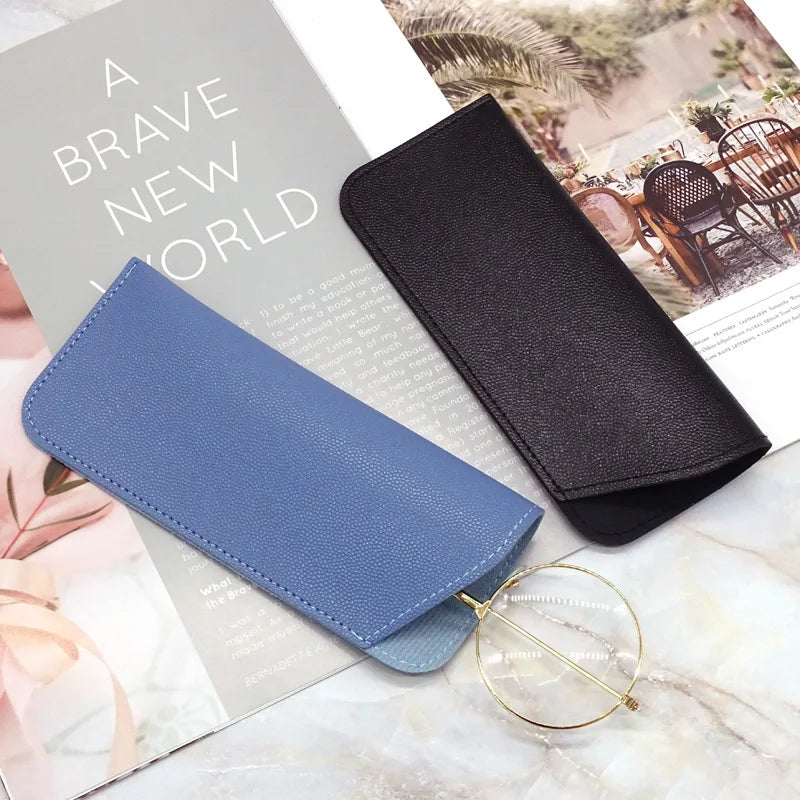 Estuche protector de cuero PU gris oscuro para gafas, apoyado en una página de revista.