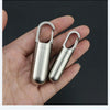A hand holds a stainless steel pill capsule with a keychain loop.