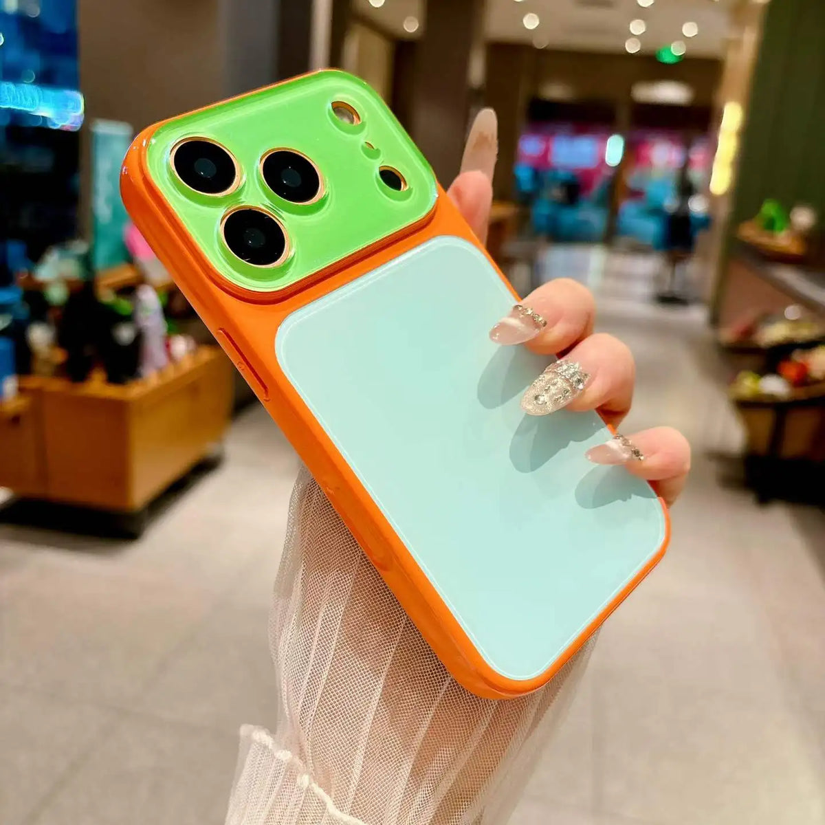 A hand holds a color blocking shockproof phone case with a bright orange frame and a light mint green back, displaying the ca