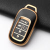A close-up view of a gold-colored Honda key fob cover with buttons and a protective case resting on a black surface.