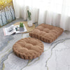 A beige corduroy floor cushion is placed on a light gray rug next to a window with sheer white curtains.