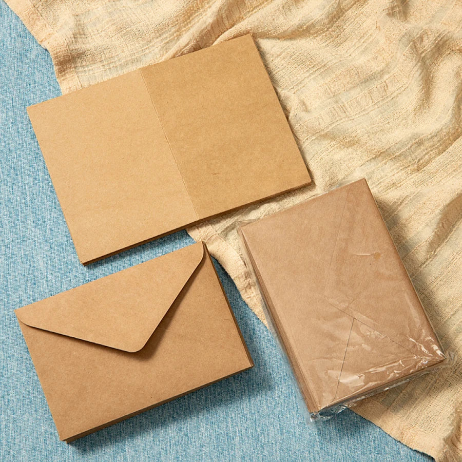 A stack of kraft paper envelopes for invitations and letters resting on a blue surface.