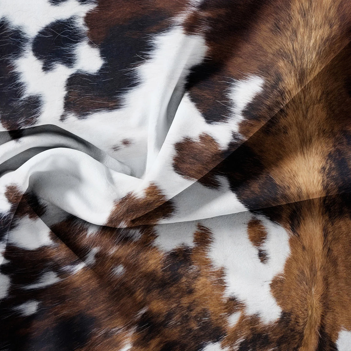 A close-up of a brown and white cow print fabric draped in soft folds.