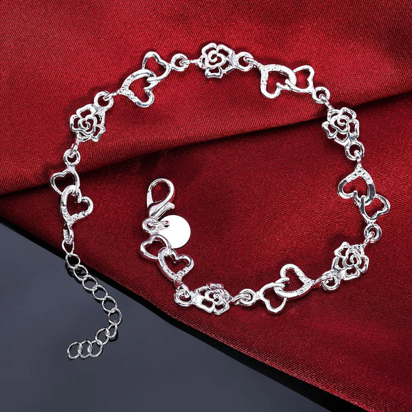 A sterling silver heart and flower chain bracelet displayed on a dark red velvet fabric.