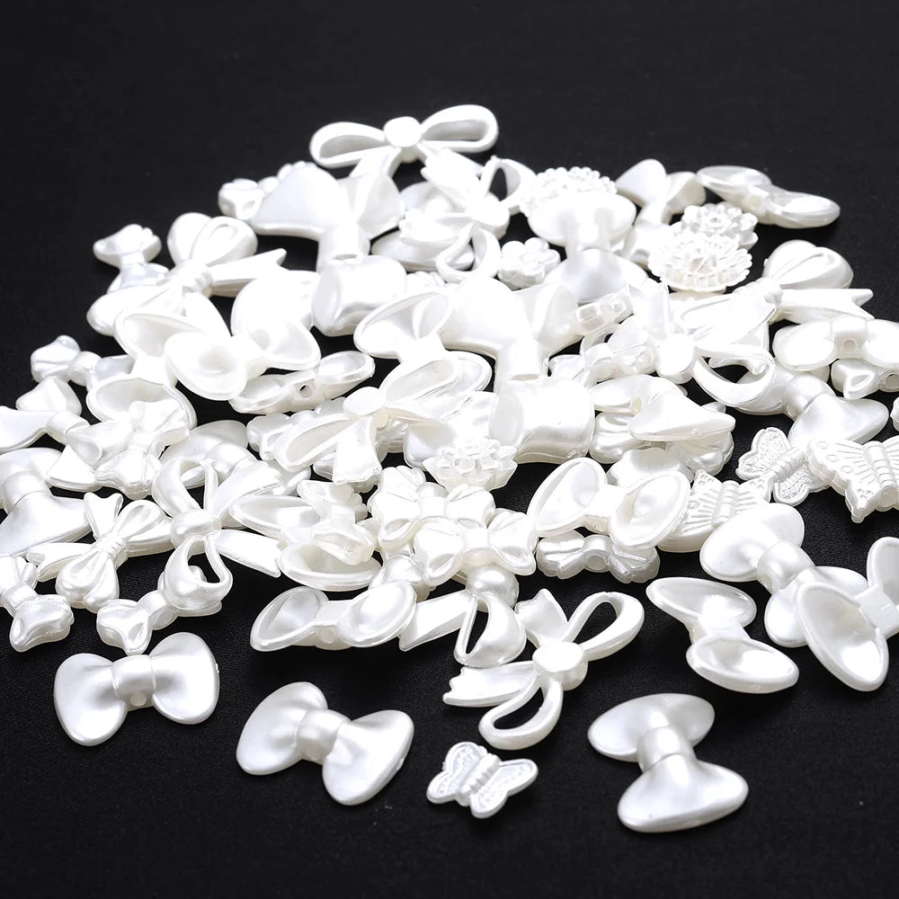 A pile of 100 white acrylic pearl spacer beads in various bow and flower shapes for jewelry making