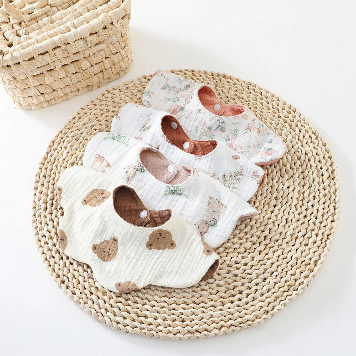 A stack of six-layer cotton baby feeding bibs with absorbent drool towels resting on a woven mat.