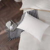 Une taie d'oreiller en soie blanche avec un jeté à motifs noir et blanc et un petit objet en céramique sur un plancher en boi