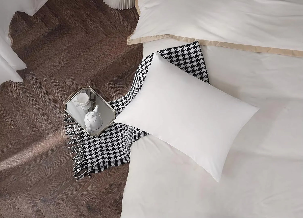 Une taie d'oreiller en soie blanche avec un jeté à motifs noir et blanc et un petit objet en céramique sur un plancher en boi