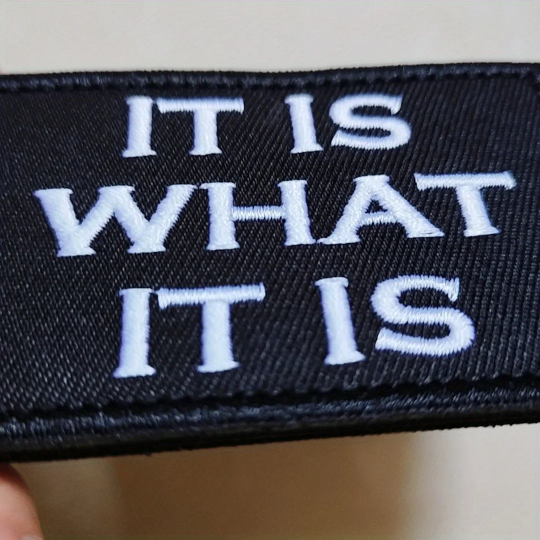 Black embroidered patch with white text reading IT IS WHAT IT IS