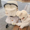 A baby wearing a beige bear-themed hooded jacket is seated in a light-colored stroller organizer.